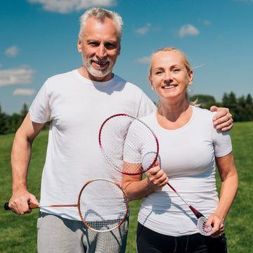 Man and woman holding badminton rackets in a grassy outdoor setting